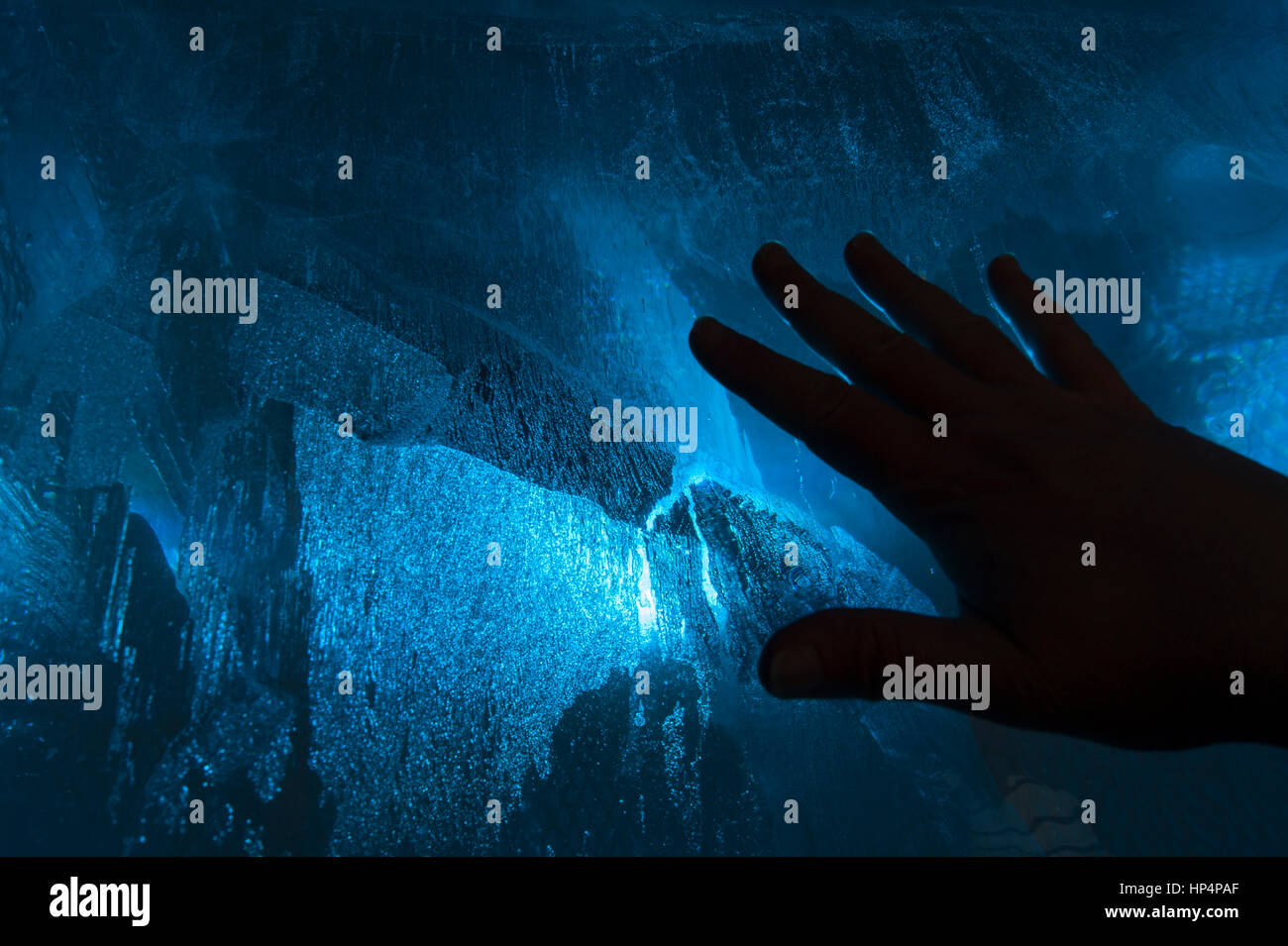 Mano su un blu freddo blocco di ghiaccio, il rapporto tra uomo e natura, tra le persone e i fenomeni naturali, il principio della termodinamica Foto Stock