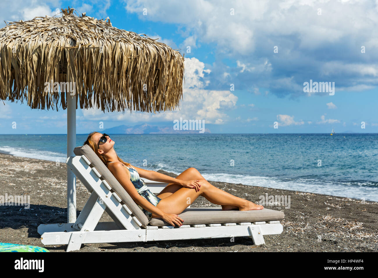 Bella giovane donna a prendere il sole sulla spiaggia in una sedia a sdraio Foto Stock