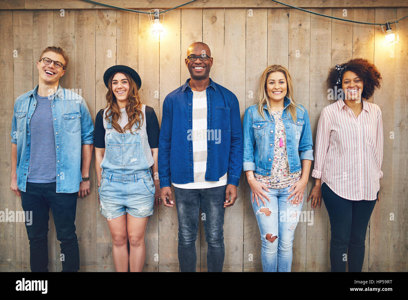 Cinque giovani uomini e donne in abbigliamento casual permanente ancora in  una fila in legno parete non verniciata, sorridente e guardando la  fotocamera Foto stock - Alamy