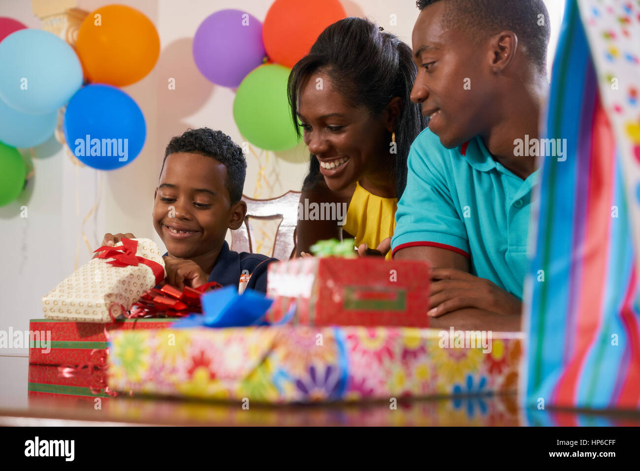 Felice famiglia nero a casa. African American padre, madre e bambino festeggia il compleanno, divertendosi a parte. Giovane ragazzo in apertura dei regali e sorridente. Foto Stock