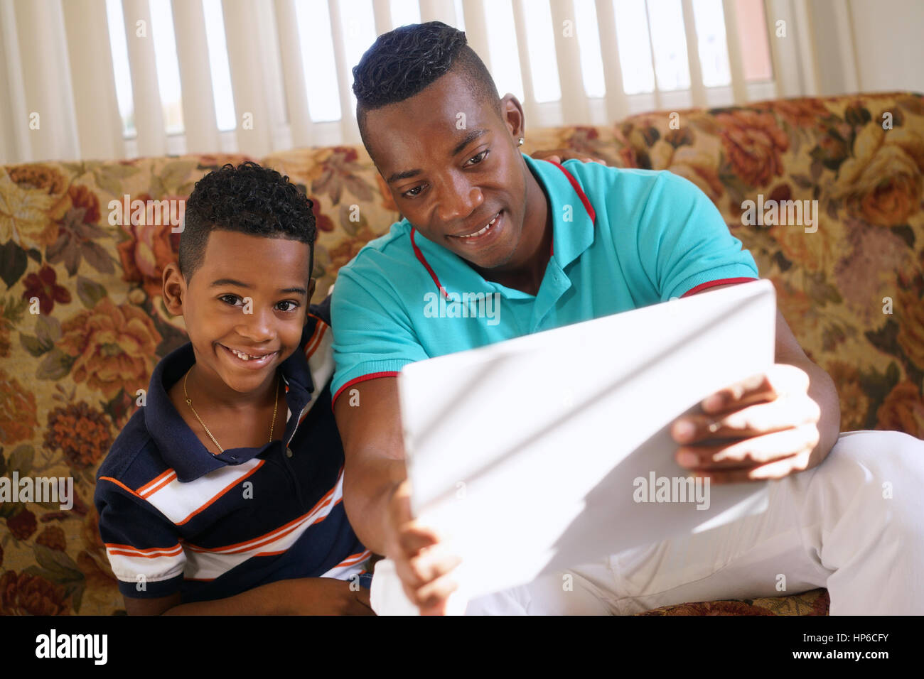 Felice famiglia nero a casa. African American padre e figlio giocando con la compressa. Papà e figlio divertendosi con il computer portatile Foto Stock