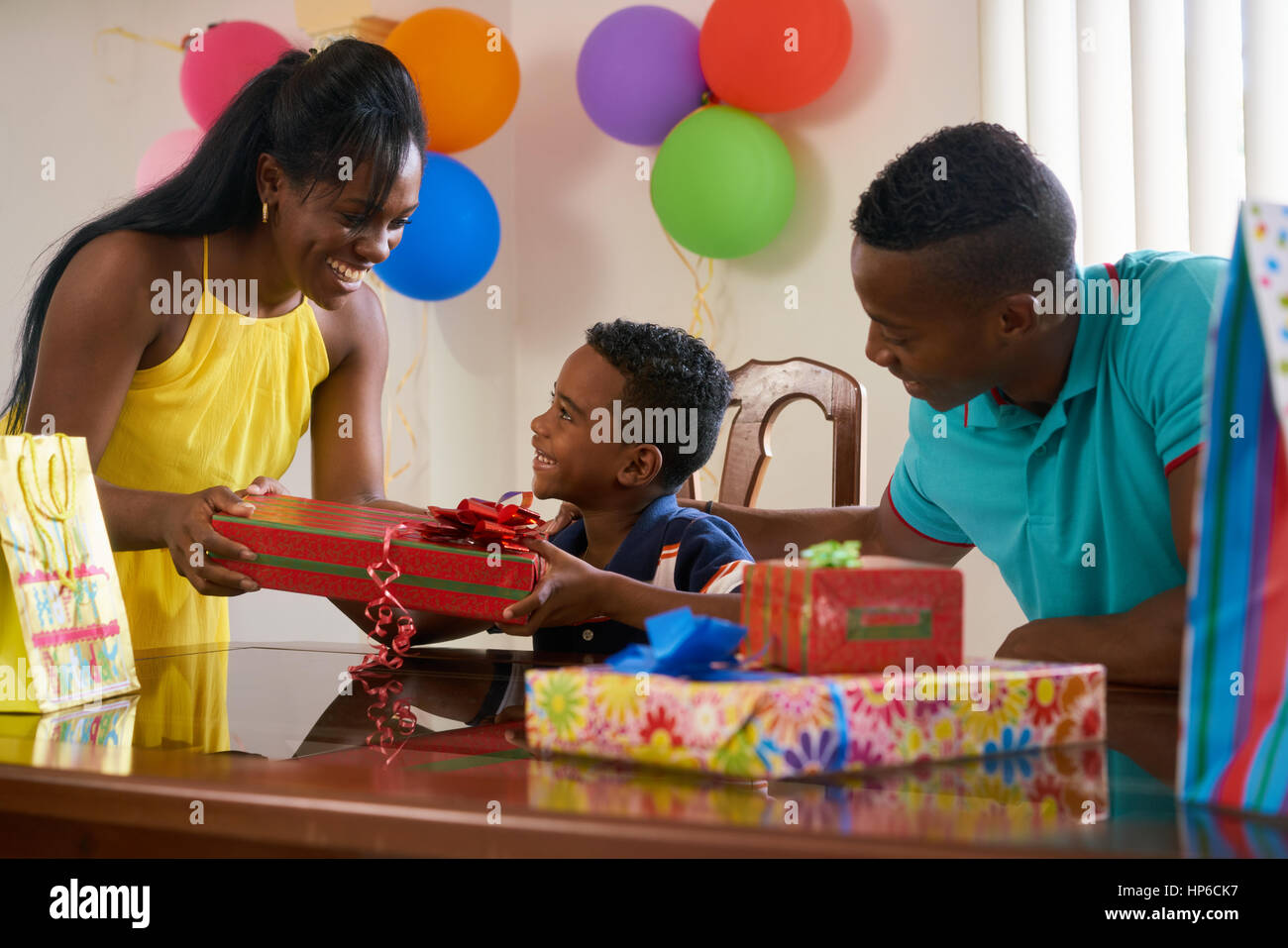 Felice famiglia nero a casa. African American padre, madre e bambino festeggia il compleanno, divertendosi a parte. Giovane donna che regalo al figlio. Foto Stock