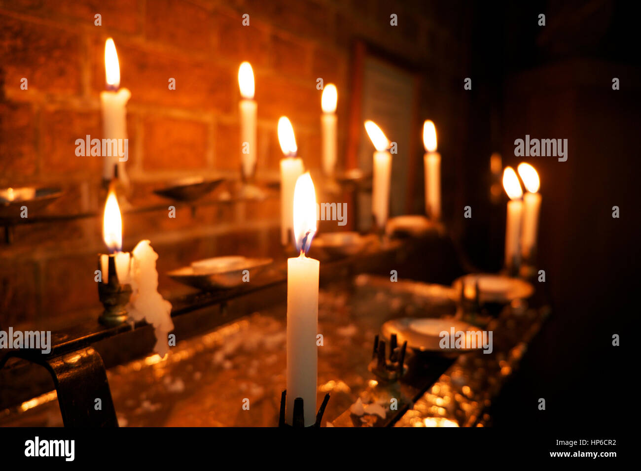 8 bruciare candele bianche in una chiesa, la candela in primo piano è a  fuoco e gli altri sono al di fuori della messa a fuoco Foto stock - Alamy
