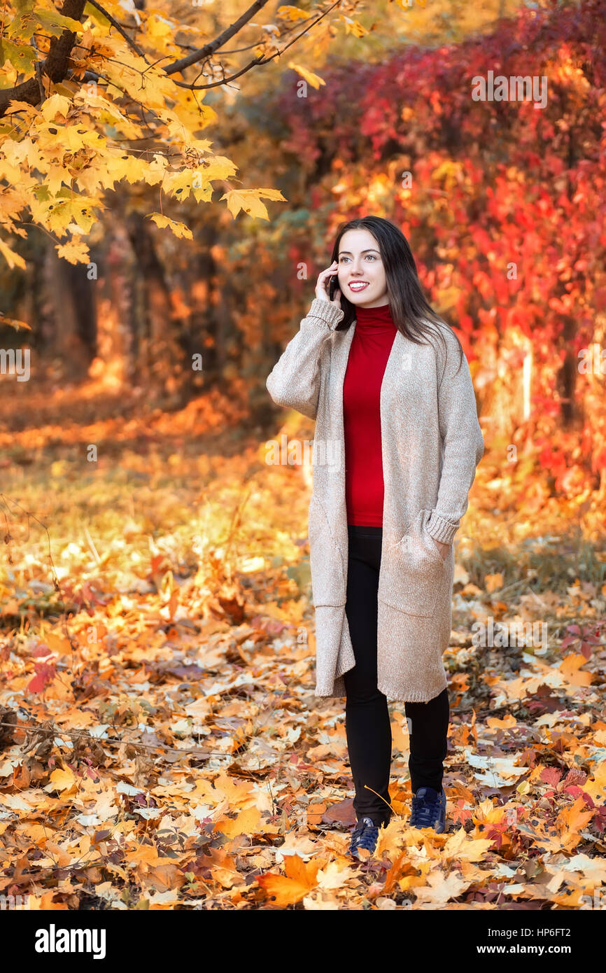 Giovane donna sorridente a piedi nel coloratissimo autunno park e parlando al cellulare. Donna allegra sta parlando su un telefono intelligente all'aperto in un luminoso lascia i Foto Stock