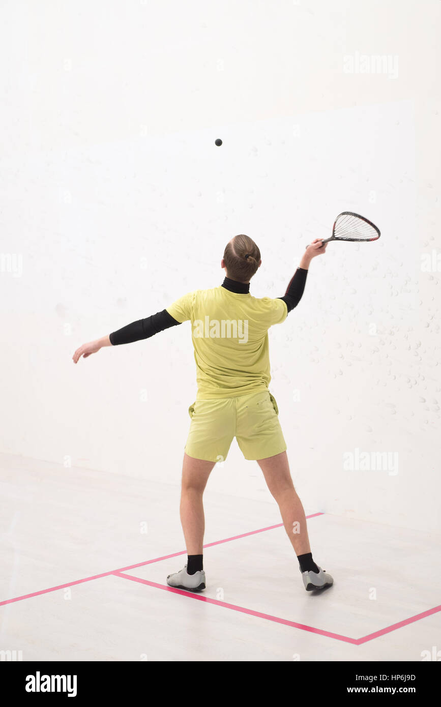Vista posteriore del giocatore di squash di colpire una palla in un campo da squash. Giocatore di squash in azione. L'uomo gioca partita di squash Foto Stock