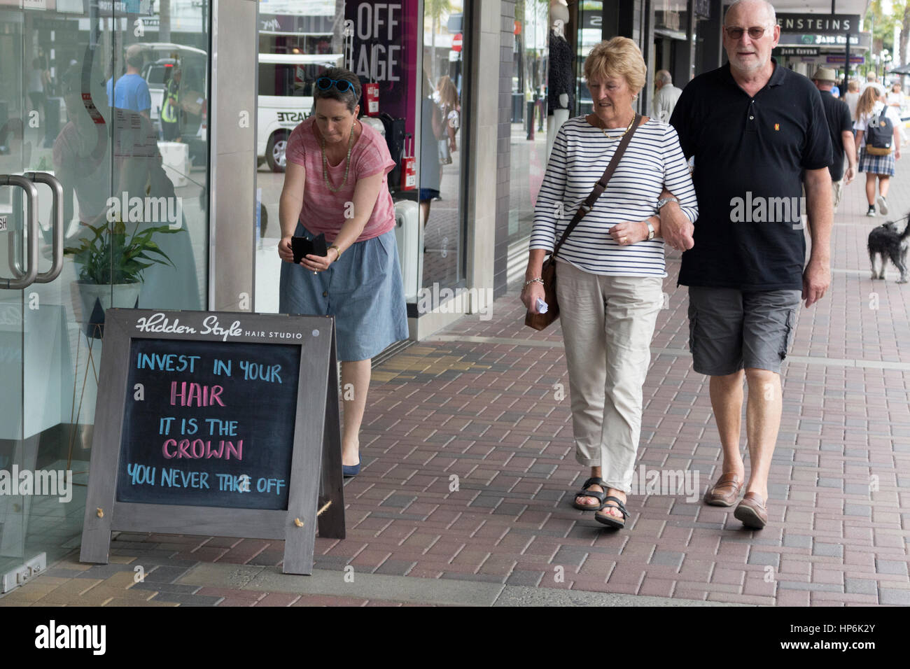 Donna con capelli corti è di scattare una foto di un divertente scheda sandwich sulla strada 'investire nei capelli' napier, Nuova Zelanda. Foto Stock