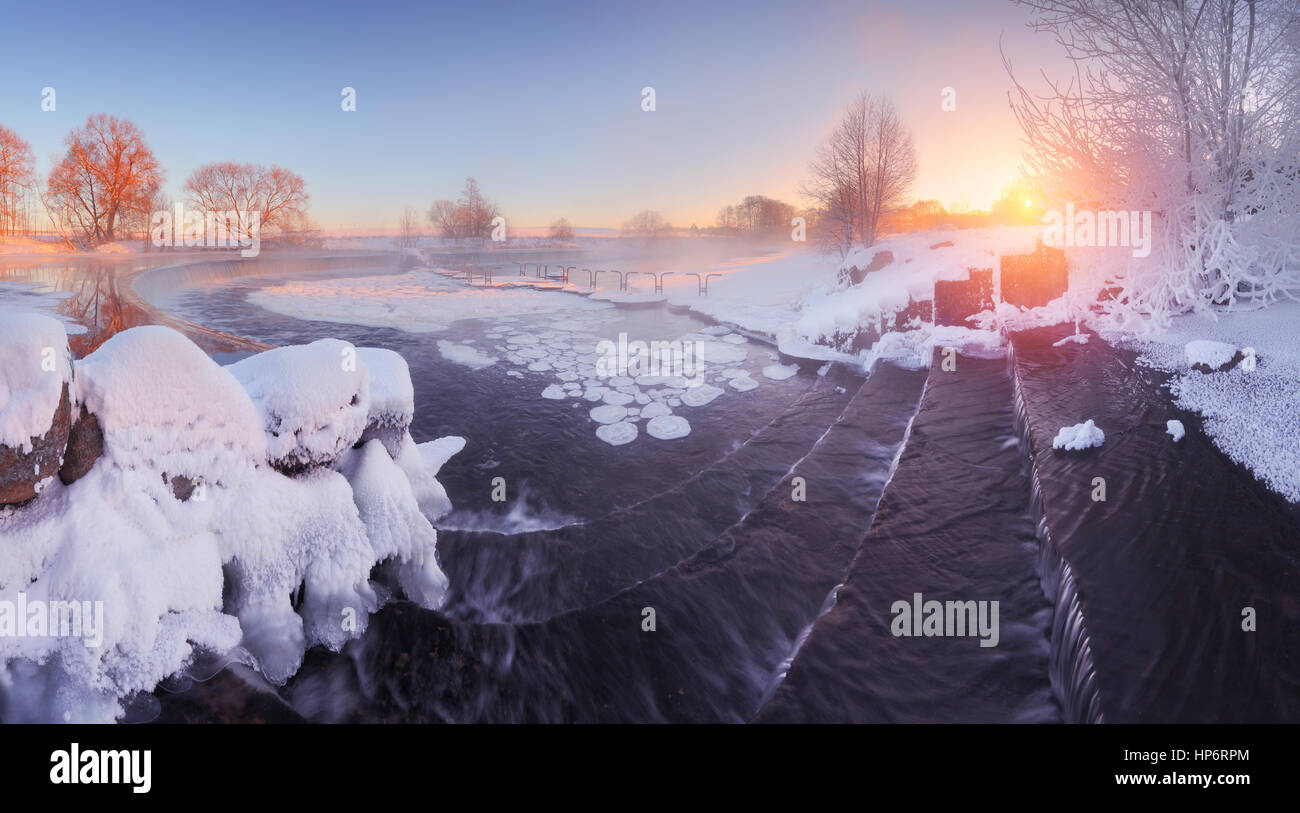 Inverno sunrise nel parco. Frosty alberi in luce del sole di mattina. Rosso brillante sole risplendere sul lago. Blu cielo d'inverno sul lago. Foto Stock