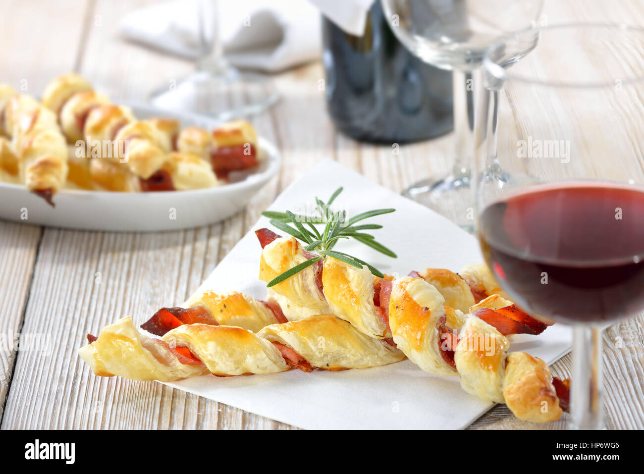 Cotta sostanziosa pasta sfoglia bastoni con prosciutto e erbe aromatiche servita con un bicchiere di vino rosso Foto Stock