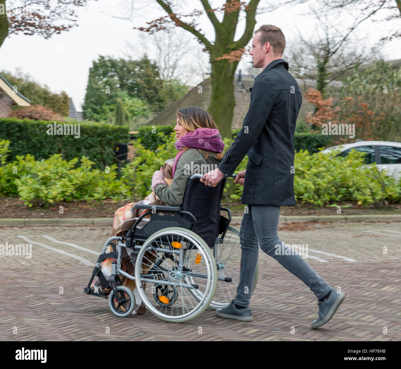 L'uomo spinge una donna su una sedia a rotelle in un posto di parcheggio in un villaggio olandese Foto Stock
