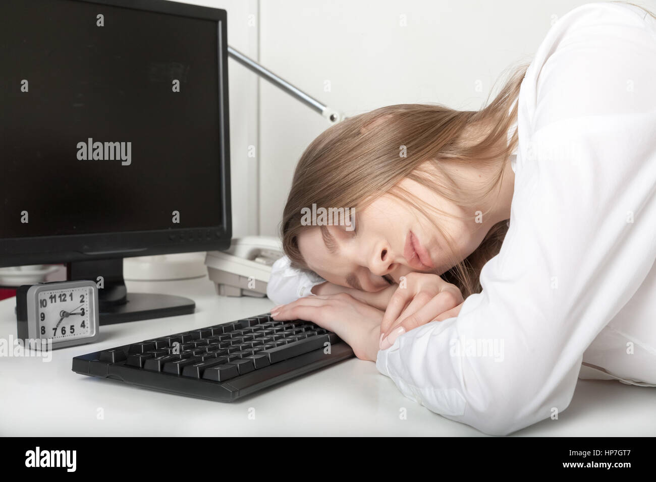 La stanca ragazza dorme in ufficio dietro una scrivania Foto Stock