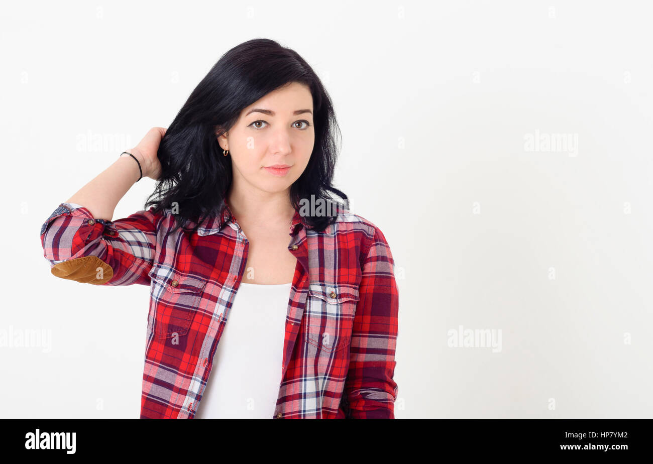 Bella ragazza in un rosso hipster plaid shirt corregge l'acconciatura pensieroso guardando la telecamera Foto Stock