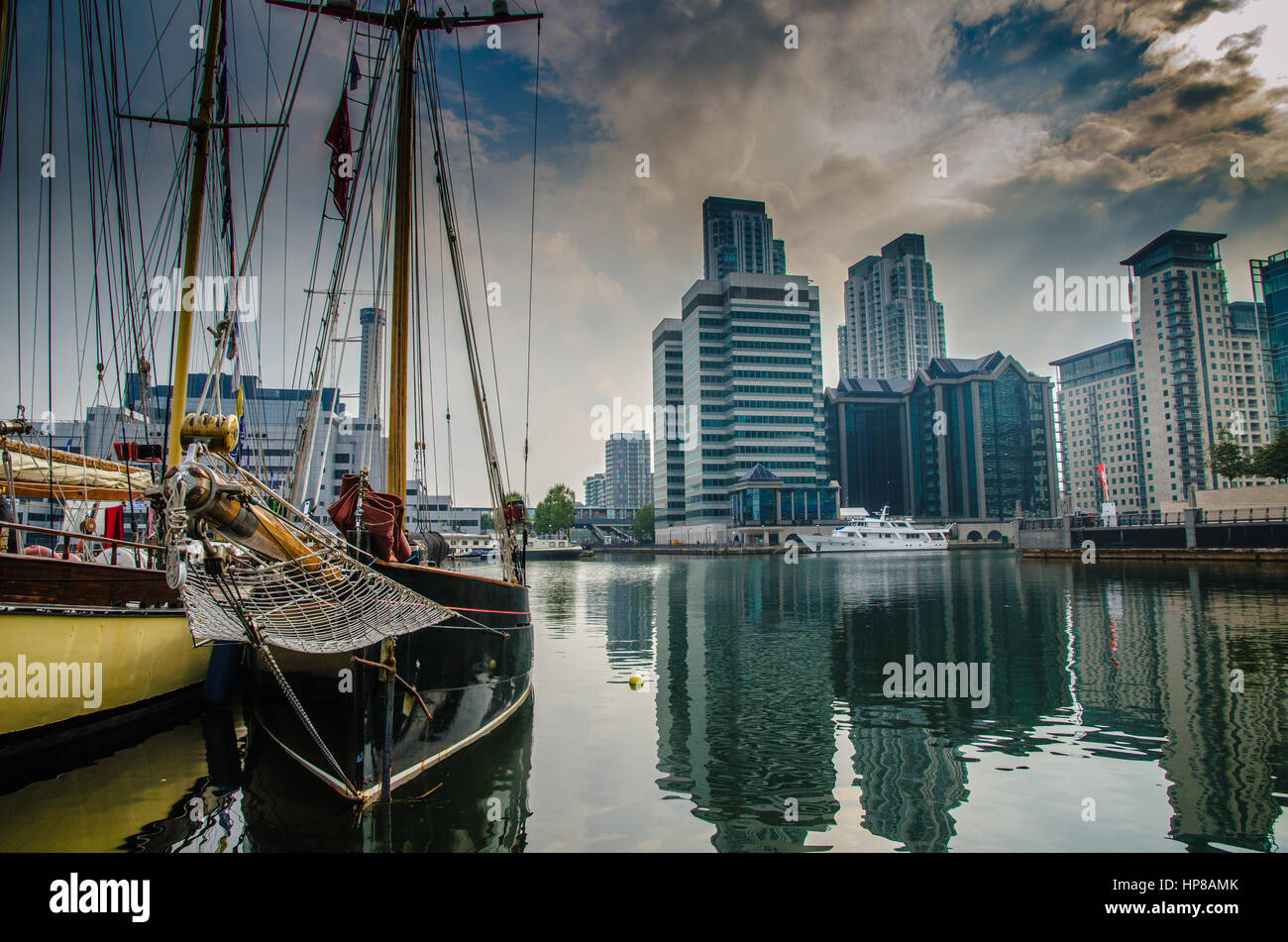 Barche, edifici per uffici e soggiorno di lusso a Londra Docklands sotto un cielo drammatico Foto Stock