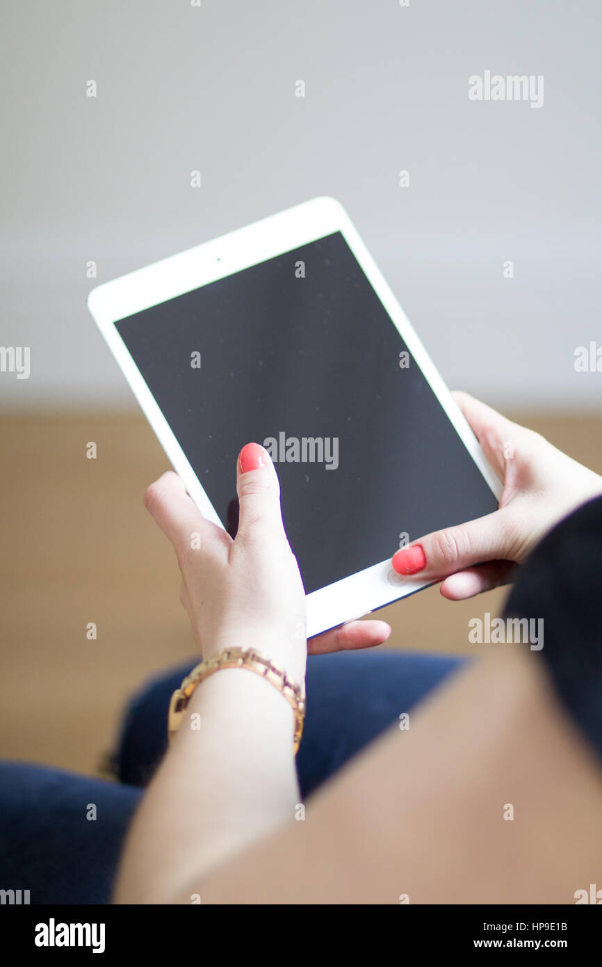 Una donna caucasica con chiodi rossi mantiene un iPad bianco Foto Stock