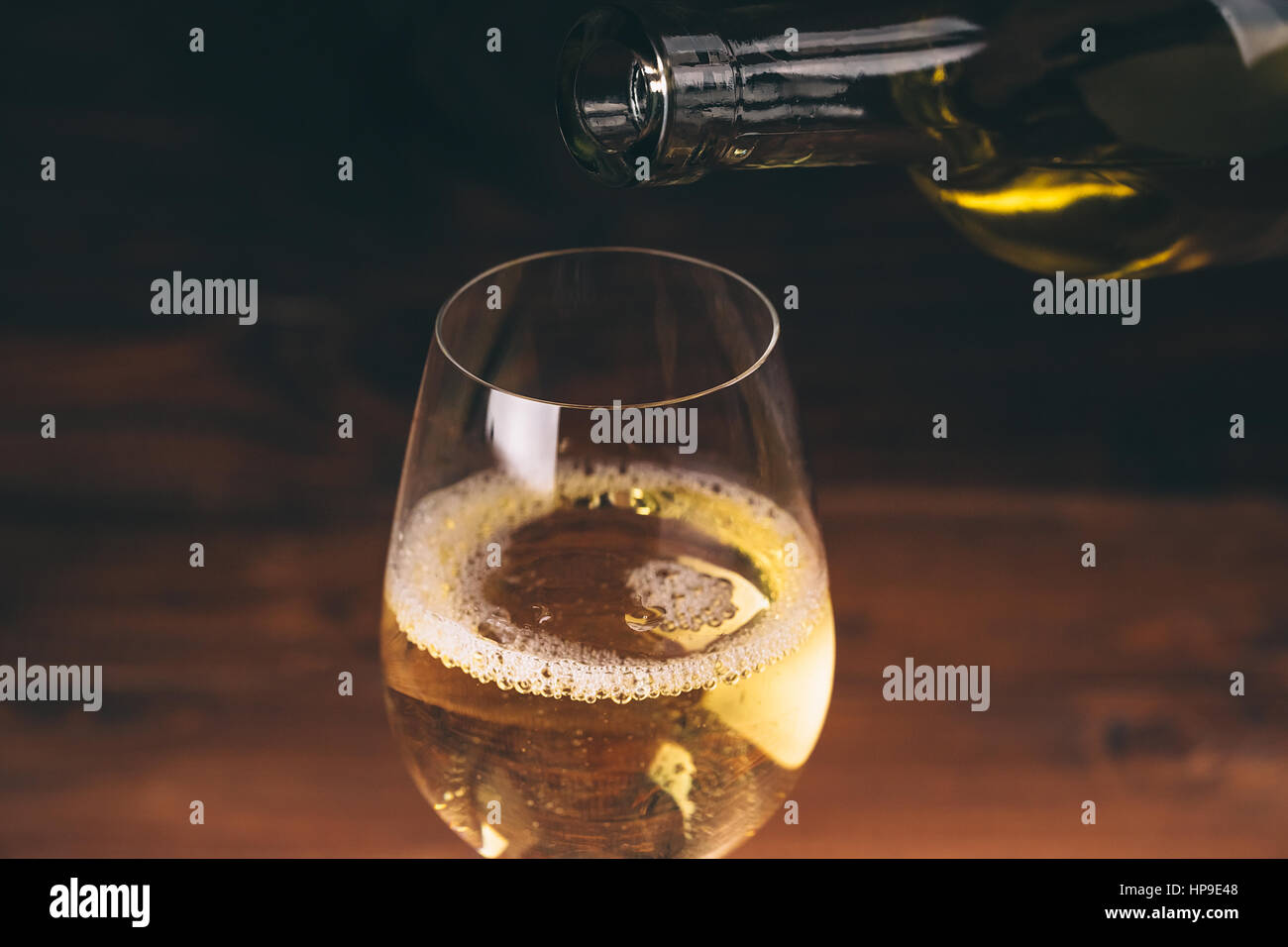 Versare il vino bianco da una bottiglia in una vista ravvicinata della wineglasses contro lo sfondo di legno Foto Stock