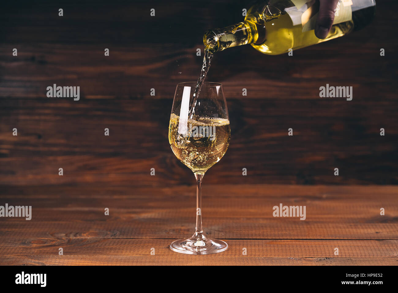 Versare il vino bianco da una bottiglia in una vista ravvicinata della wineglasses contro lo sfondo di legno Foto Stock