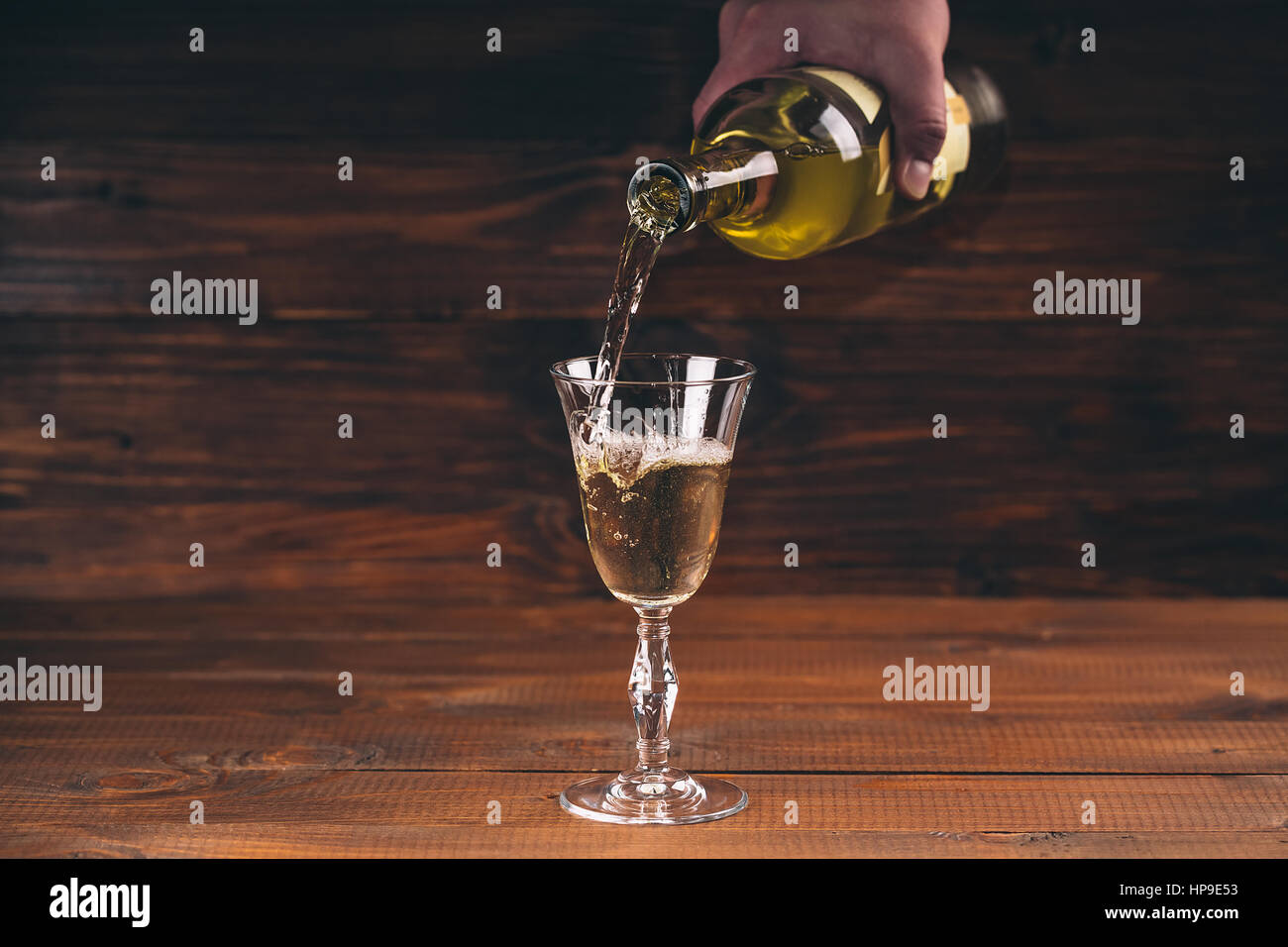 Versare il vino bianco da una bottiglia in una vista ravvicinata della wineglasses contro lo sfondo di legno Foto Stock