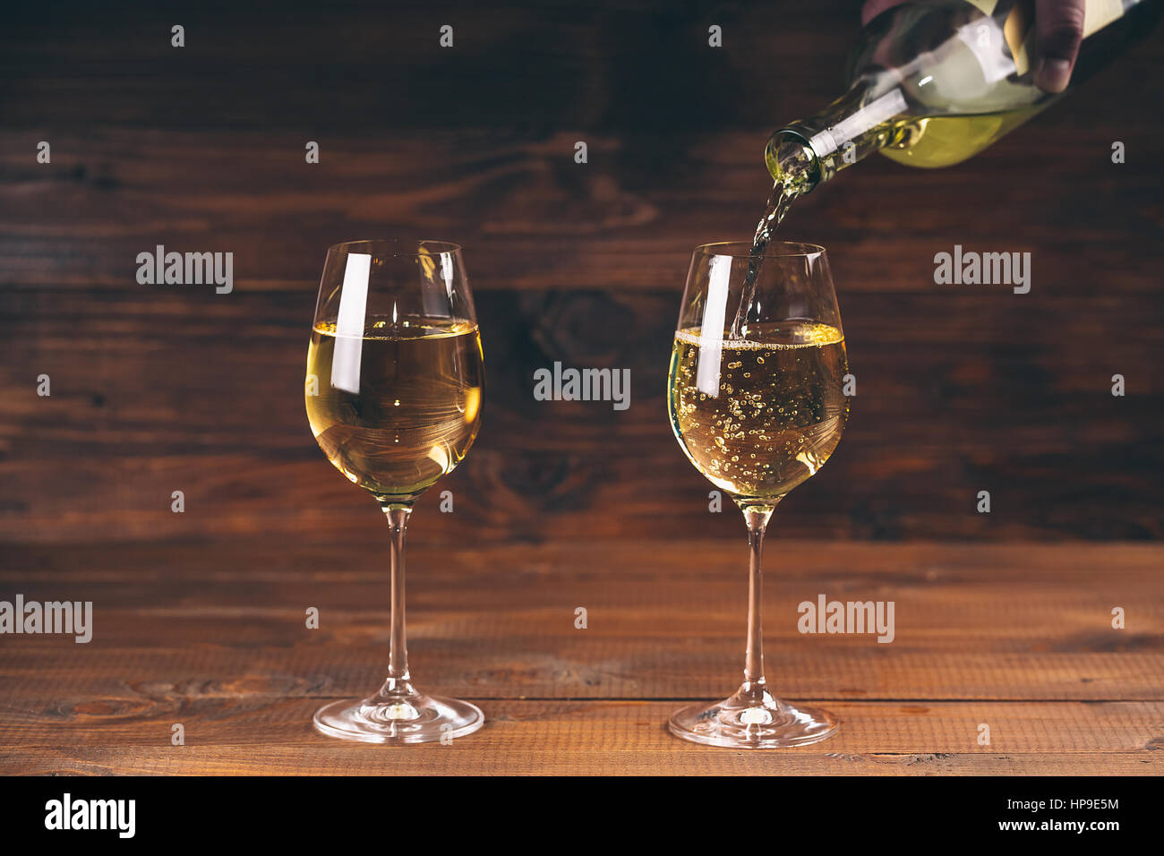 Versare il vino bianco da una bottiglia in una vista ravvicinata dei due wineglasses contro lo sfondo di legno Foto Stock