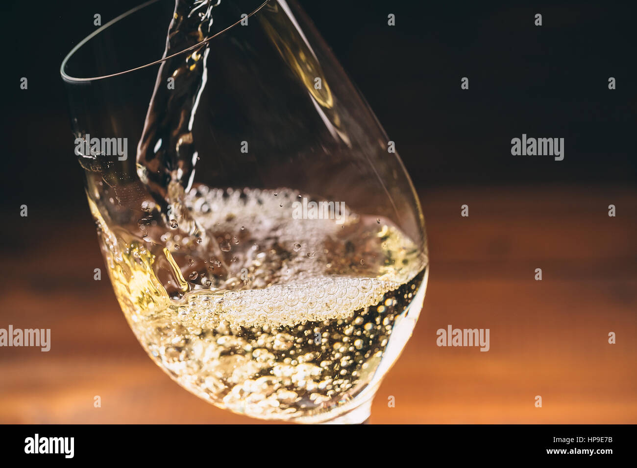 Versare il vino bianco da una bottiglia in una vista ravvicinata della wineglasses contro lo sfondo di legno Foto Stock