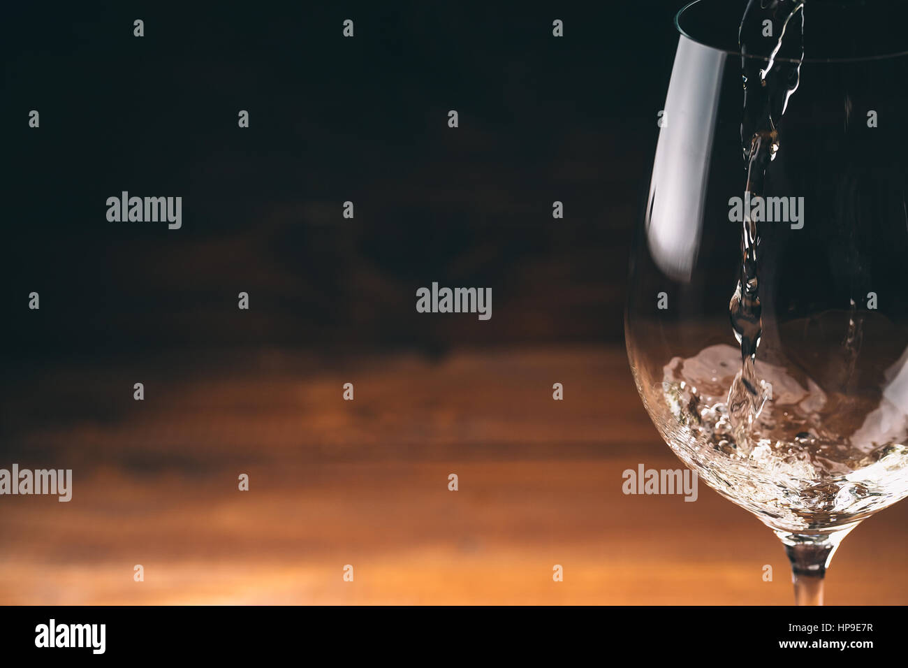 Versare il vino bianco da una bottiglia in una vista ravvicinata della wineglasses contro lo sfondo di legno Foto Stock