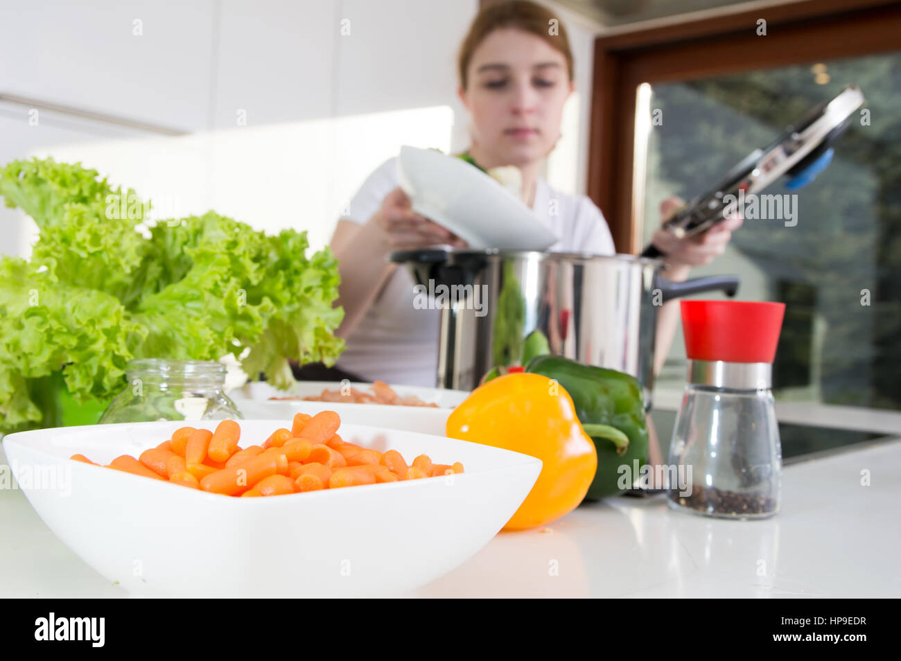 Baby carote e una donna verdure di cottura in pentola a pressione sullo sfondo. Foto Stock