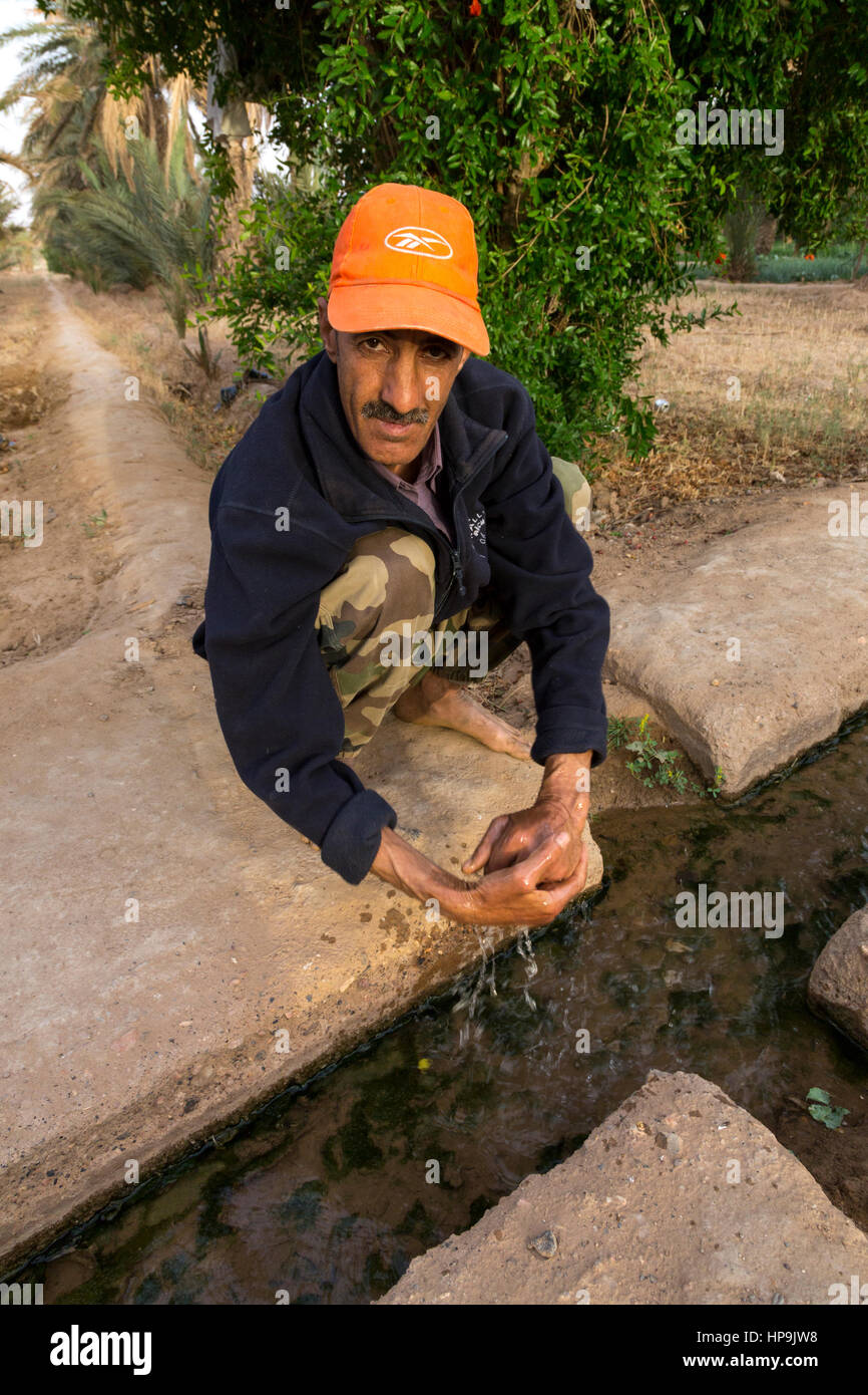 Merzouga, Marocco. Agricoltore lavarsi le mani nel canale di irrigazione che trasportano l'acqua per gli agricoltori' tenute nell'oasi di Merzouga. Foto Stock