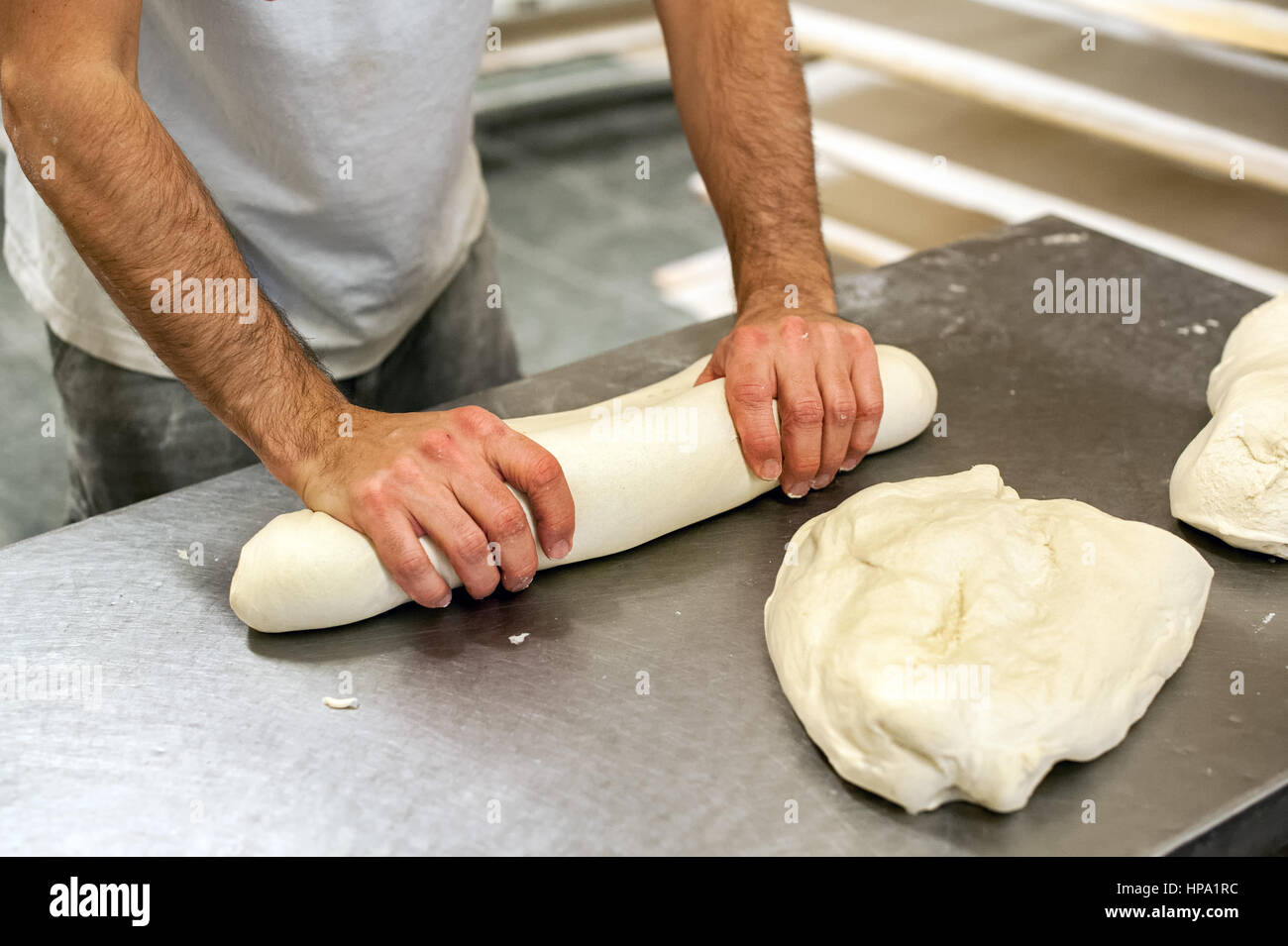 Close-up immagine del panettiere del maschio in t-shirt e per impastare la pasta di rotolamento carteggiatura al tavolo da forno con lucida la superficie di metallo Foto Stock