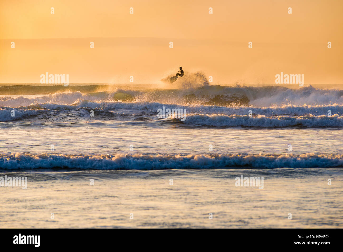 Surfer in azione e la cattura di un po' di aria dopo aver colpito la cresta di un'onda a Godrevy baia del sole invernale.surfer oscurati da ombre in modo non identificabile Foto Stock