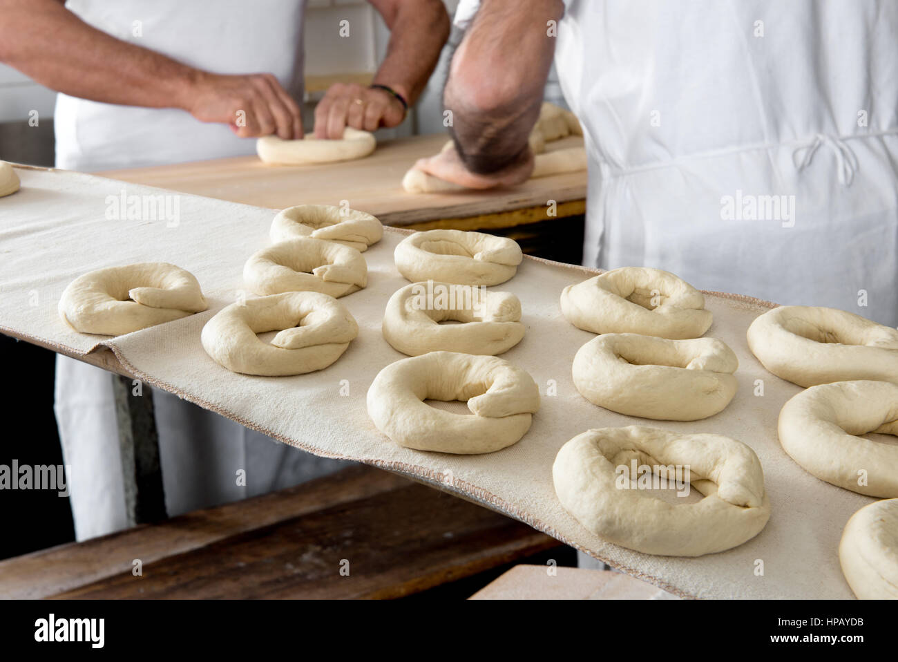 Close-up di a forma di ciambella di pezzi di impasto su tavola, il procedimento di preparazione di pane frisella dai panettieri maschio in background Foto Stock