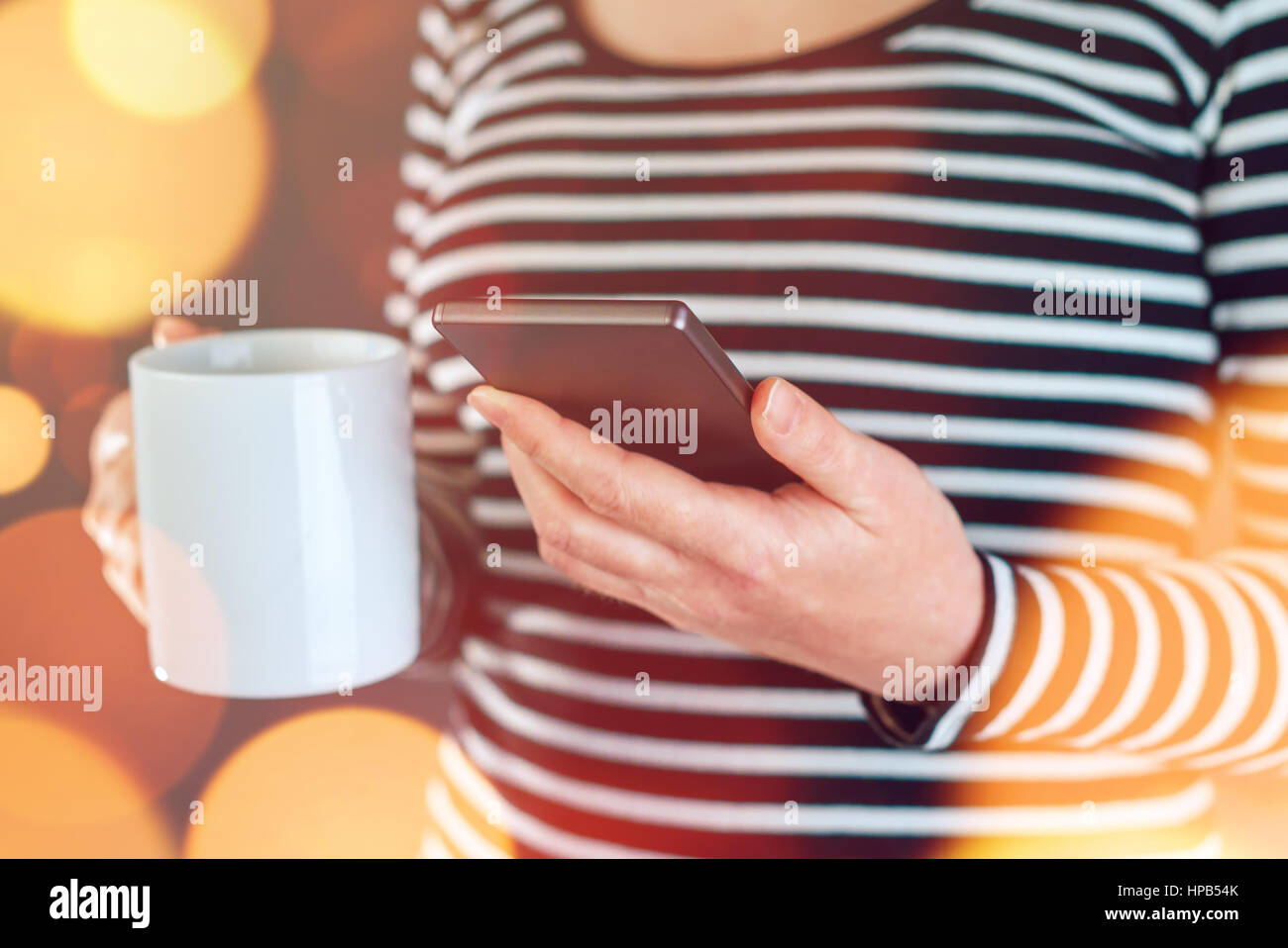 Donna informale per leggere le notizie sul telefono cellulare e di bere il caffè come parte delle attività quotidiane di routine mattutina Foto Stock