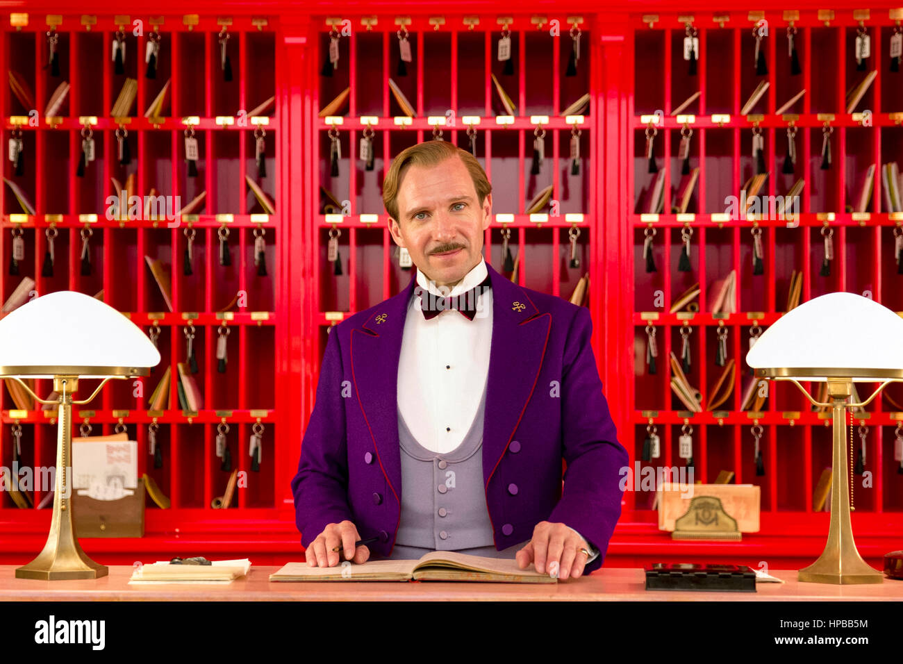 Monsieur Gustave H. (Ralph Fiennes) il leggendario concierge presso la reception in 'Il Grand Hotel di Budapest" (2014) diretto da Wes Anderson. Foto Stock