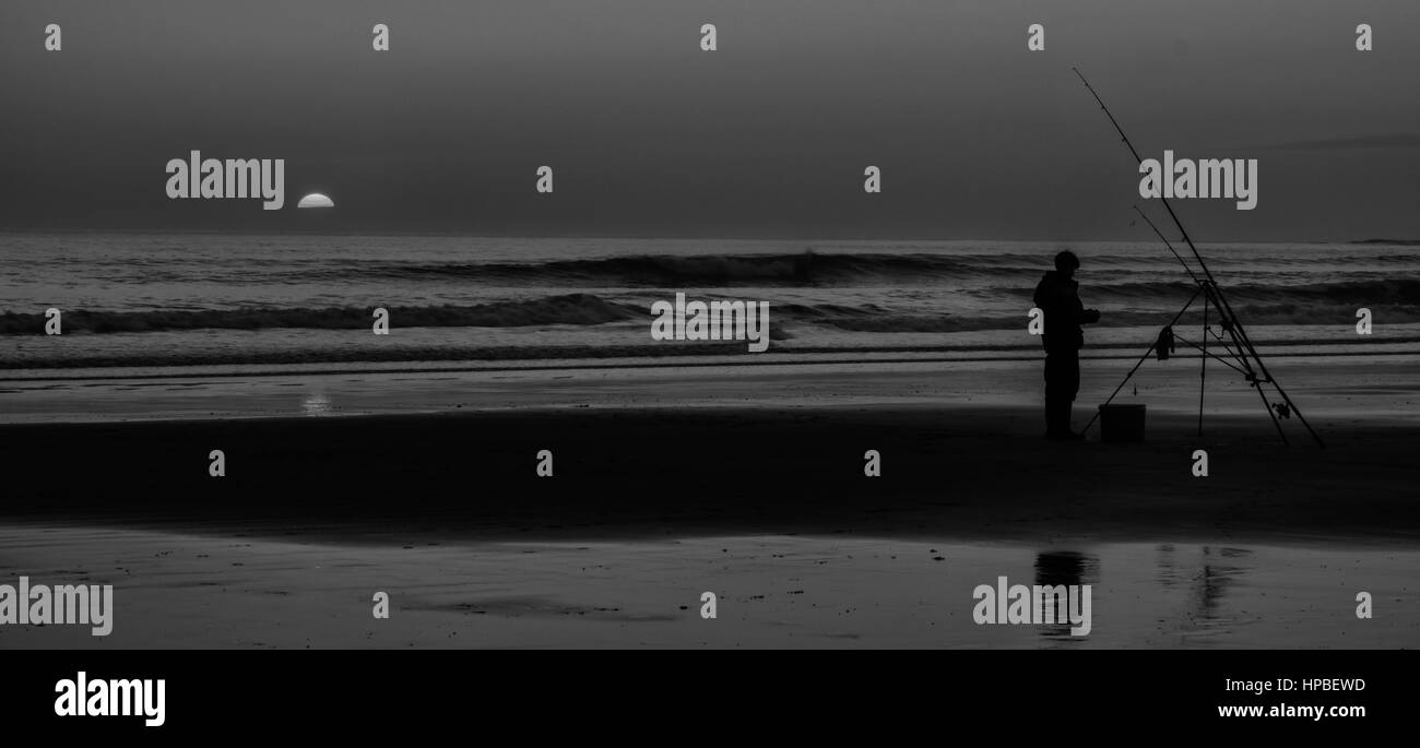 La cattura di un tramonto sulla spiaggia di Baia Trecco vicino Porthcawl in Galles. Da soli Fisherman sperando per una cattura come i tramonti Foto Stock