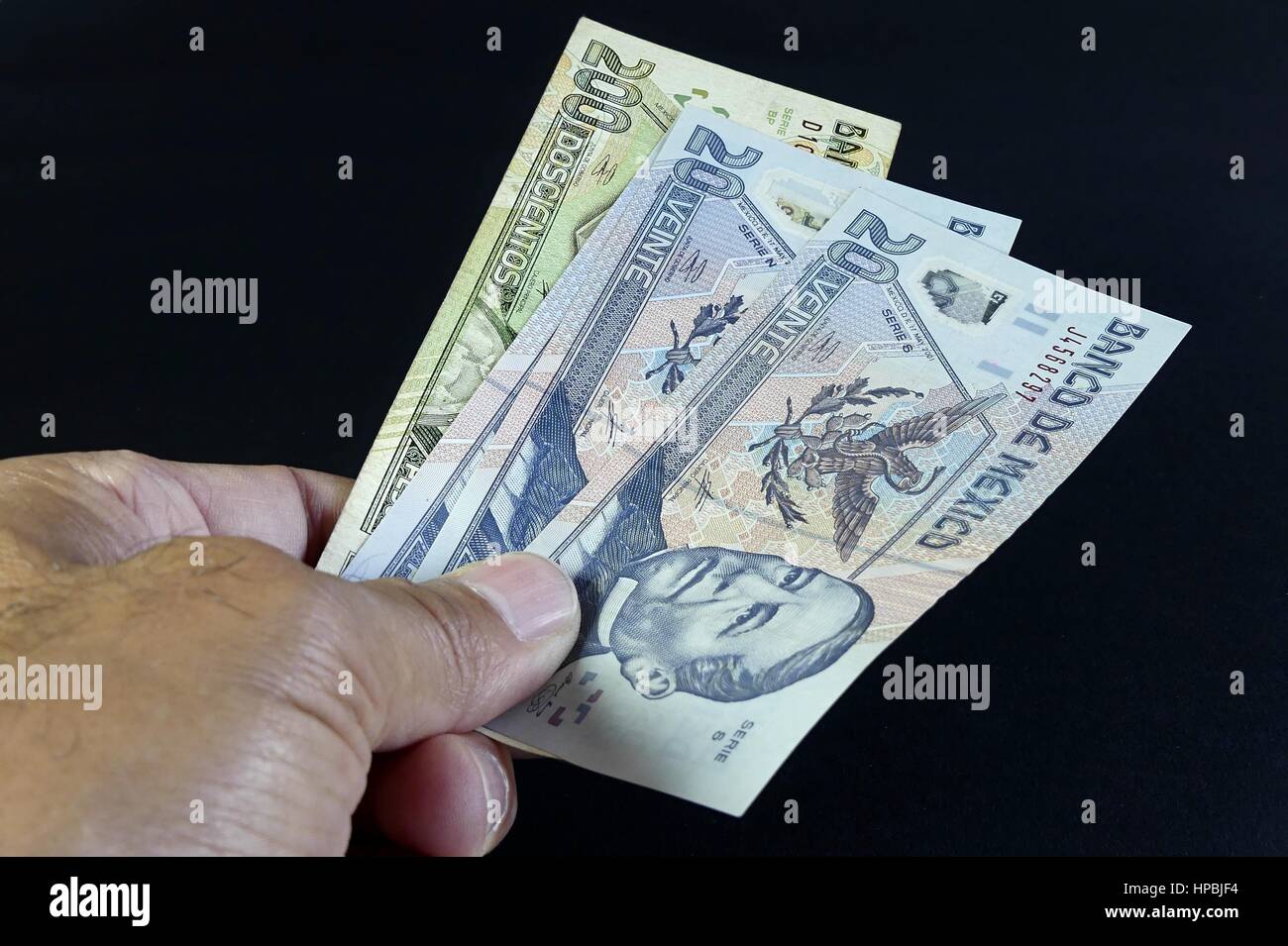 Isolato mano di uomo dando il Messico Pesos su sfondo nero Foto Stock