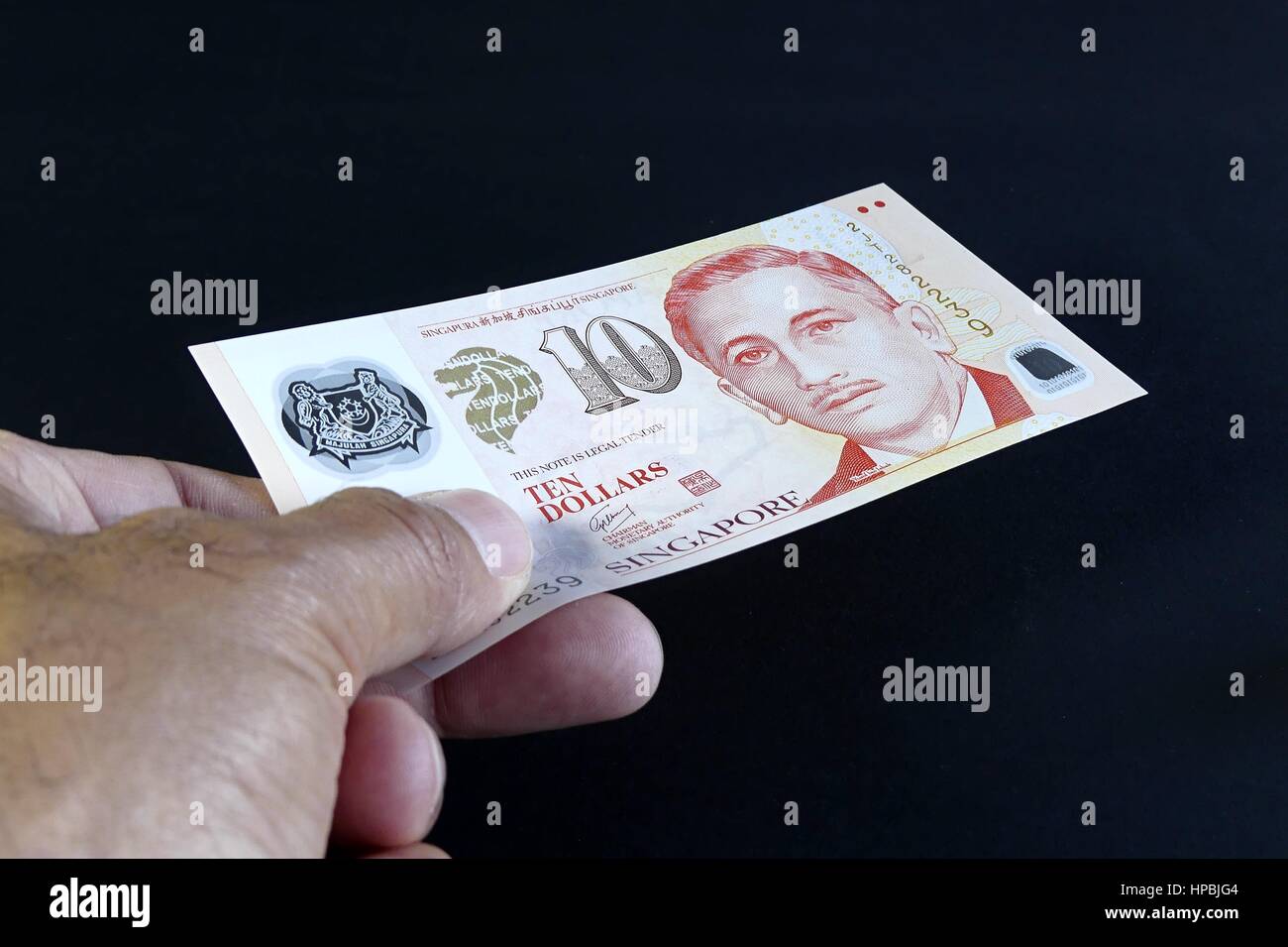 Isolato mano di uomo dando dollari di Singapore su sfondo nero Foto Stock