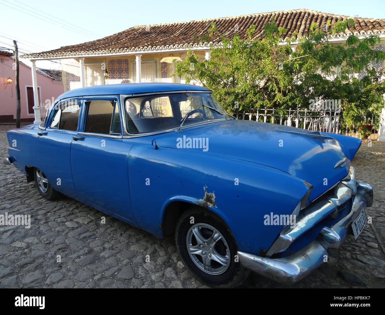 Classic american auto blu parcheggiata su una strada a ciottoli in Trinidad, Cuba con i vecchi edifici coloniali sullo sfondo Foto Stock
