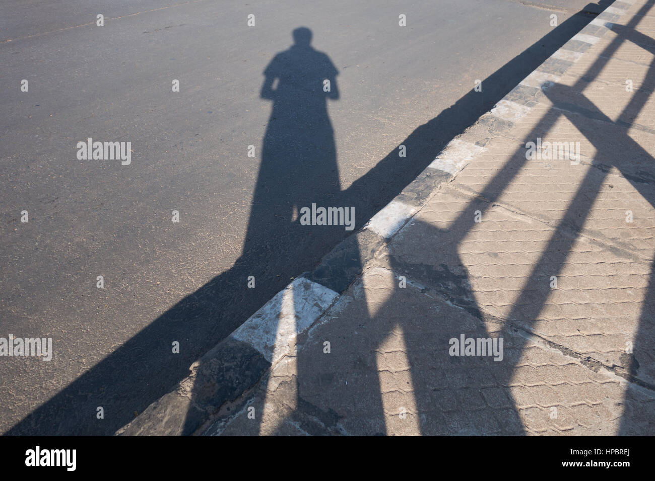 Uomo indiano di scattare una foto della propria ombra in piedi su un marciapiede accanto alla ringhiera in Hyderabad, India Foto Stock