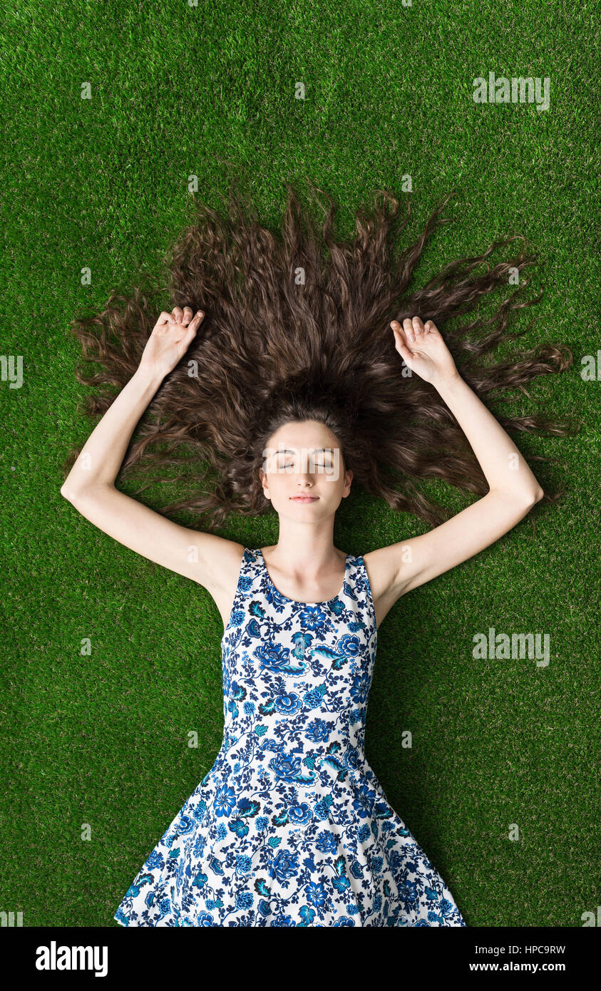 Ragazza giovane sdraiati sull'erba con i suoi lunghi capelli sparsi, lei sta dormendo e rilassante Foto Stock