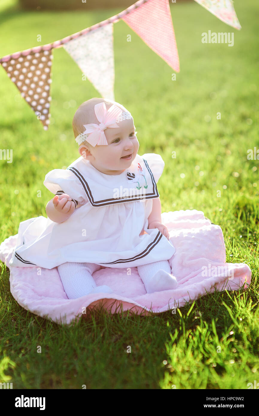 Bambina in abito bianco seduto sull'erba nel parco Foto Stock
