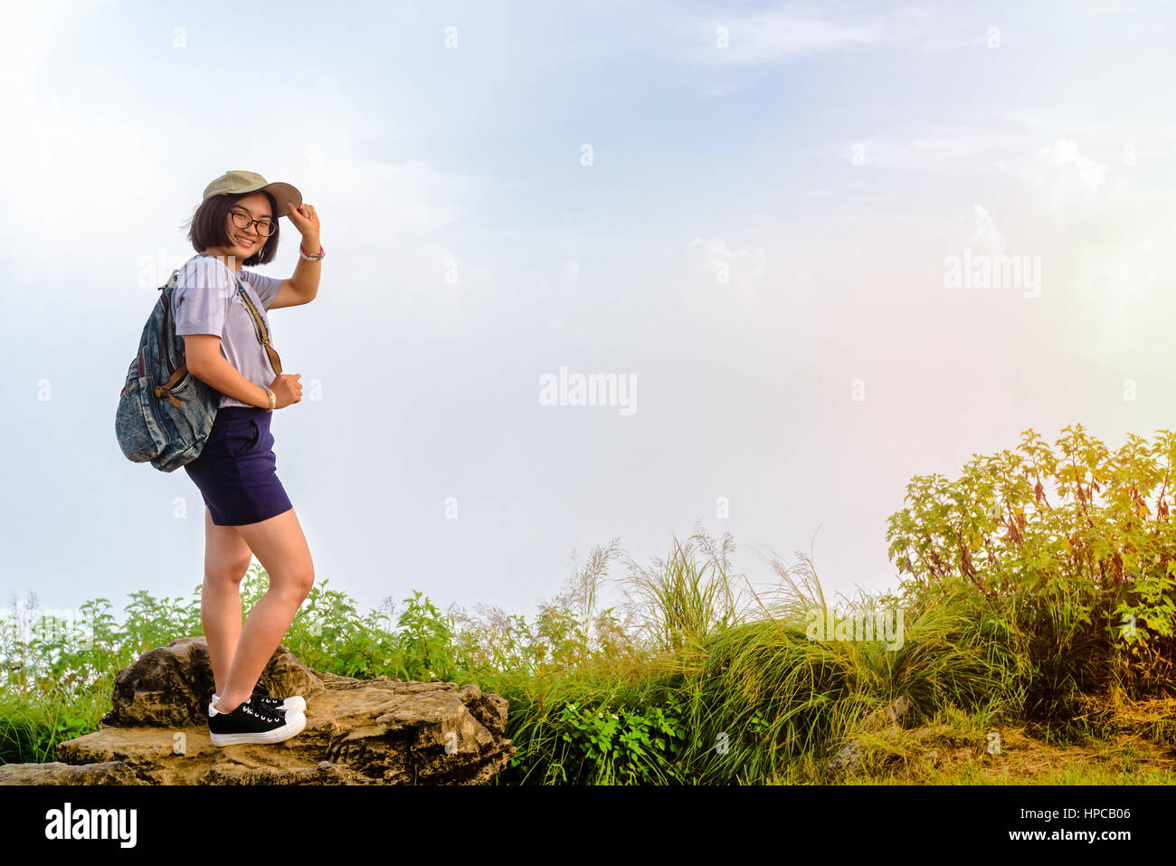 Tourist teens ragazza escursionista con zaino cappello e occhiali è sorriso permanente e pone felicemente in alta montagna su sky e lo sfondo di nebbia al punto panoramico Foto Stock