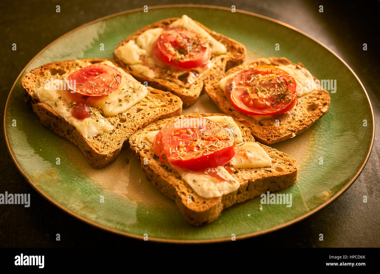 Il formaggio fuso su pane tostato con fette di pomodoro e le erbe aromatiche Foto Stock