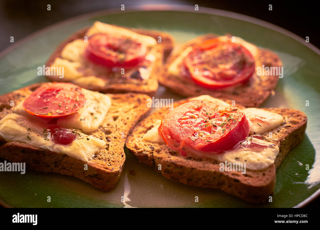 Il formaggio fuso su pane tostato con fette di pomodoro e le erbe aromatiche Foto Stock