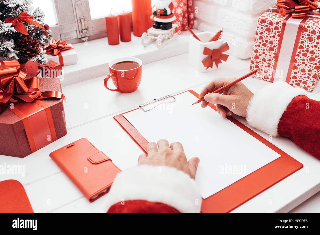 Babbo Natale a lavorare alla scrivania e scrivere su un foglio bianco su una clipboard, egli è sempre pronto per il Natale Foto Stock