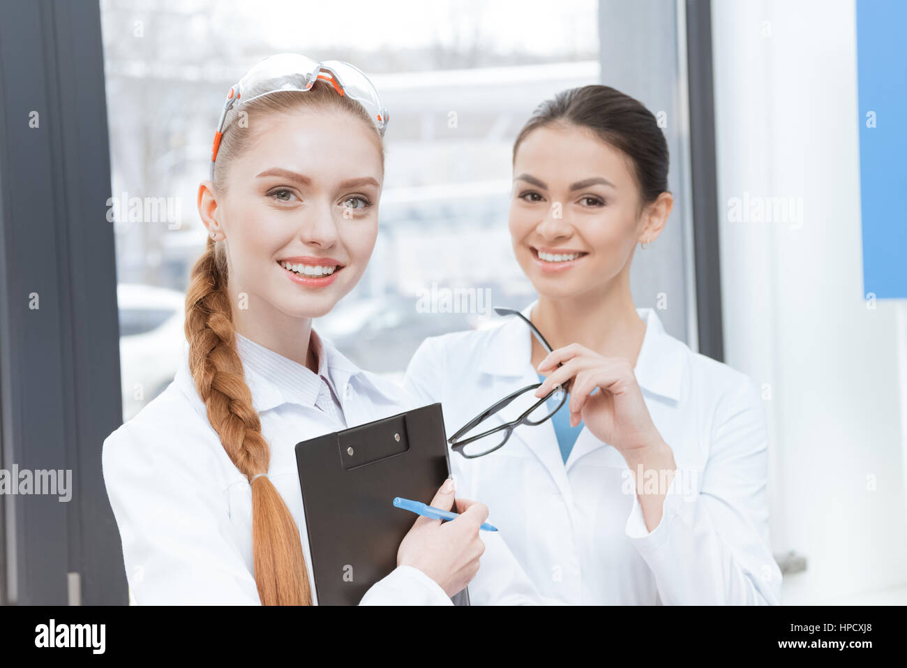 Le giovani ricercatrici in camici sorridente in telecamera in laboratorio Foto Stock