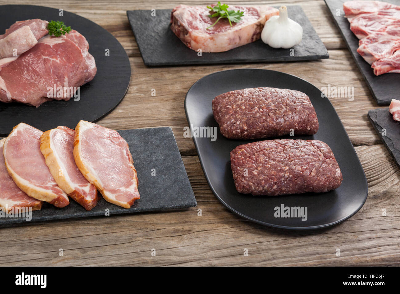 Varietà di carne sul vassoio nero contro lo sfondo di legno Foto Stock