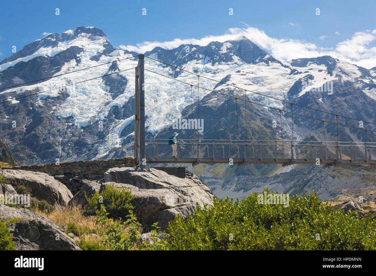 Dal Parco Nazionale Aoraki/Mount Cook, Canterbury, Nuova Zelanda. Escursionista attraversando un ponte sospeso su il Hooker Valley via, Mount Sefton in background. Foto Stock