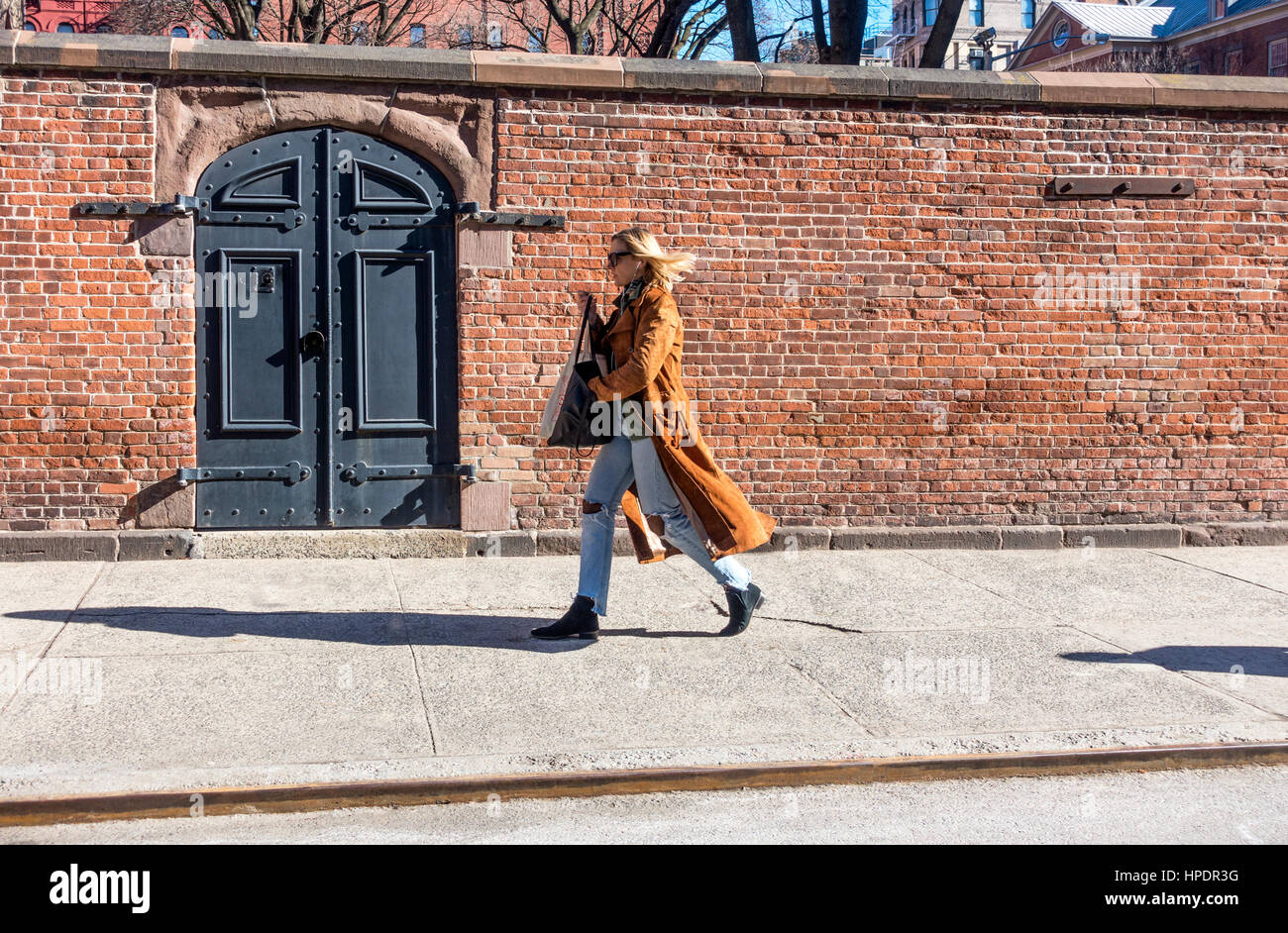 Elegante Donna che cammina veloce nel tagliare jeans e lungo cappotto su Mulberry Street in Nolita, NYC Foto Stock