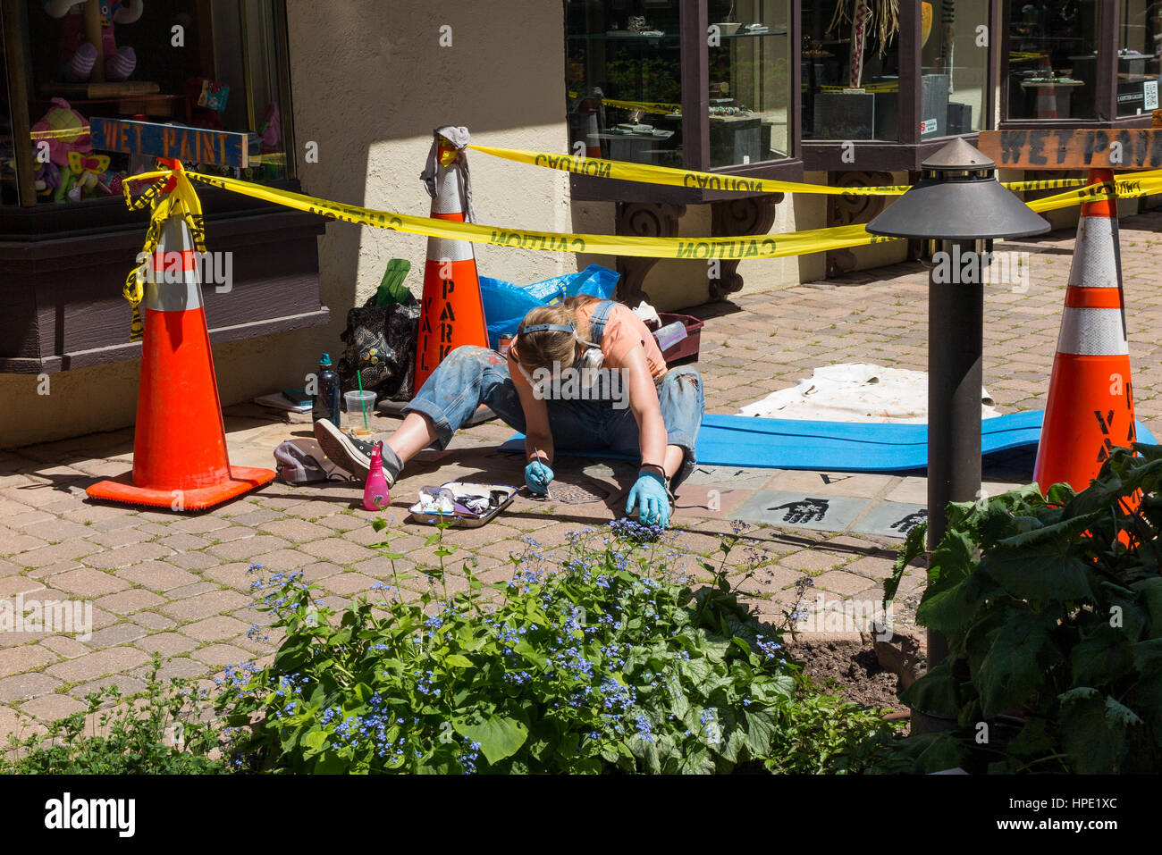Giovane donna / artista indossare un respiratore di protezione durante la pittura a mano Arte / decorazioni su un marciapiede Foto Stock