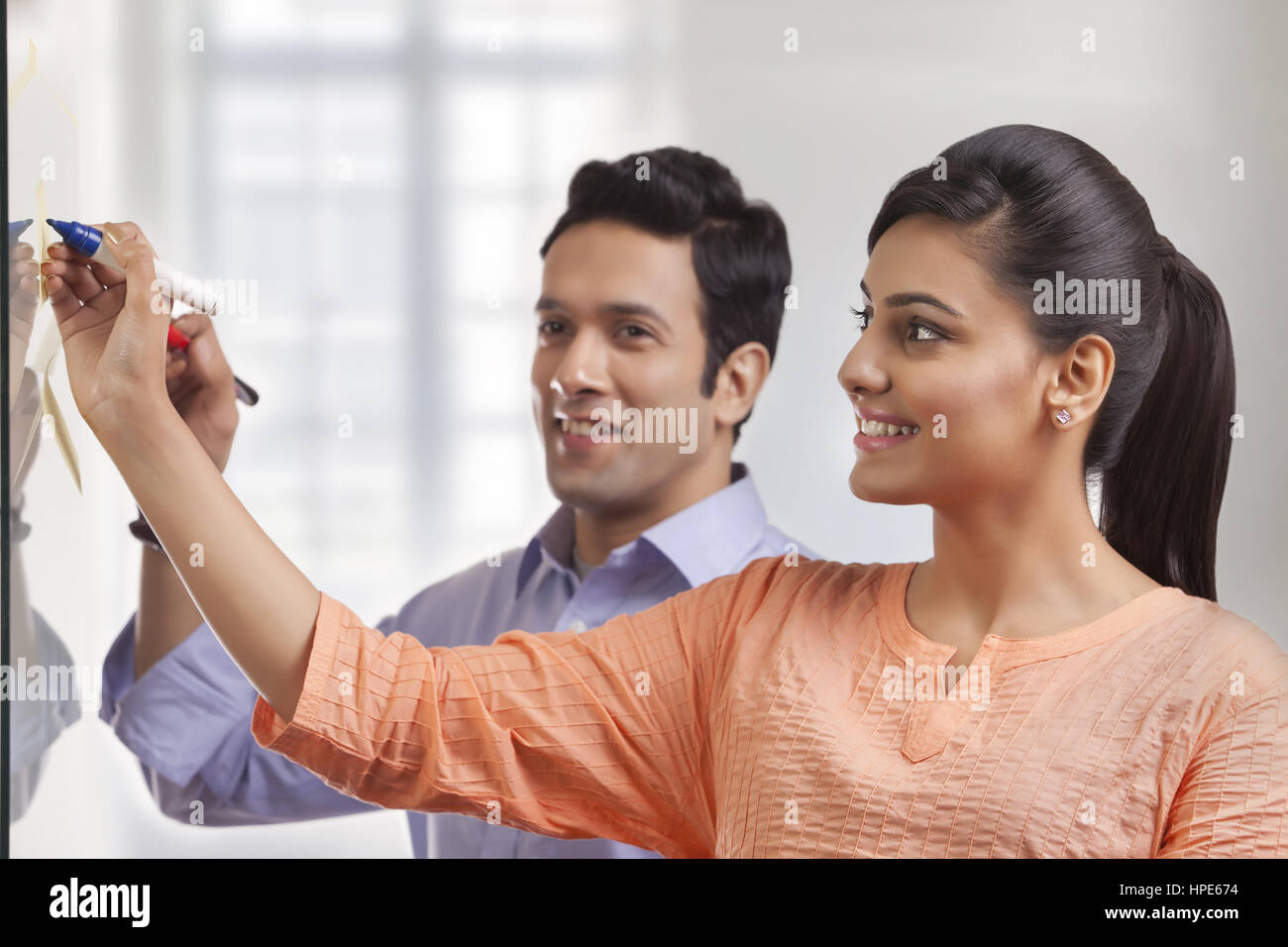 Due colleghi sorridente in ufficio scrivendo su una lavagna bianca Foto Stock