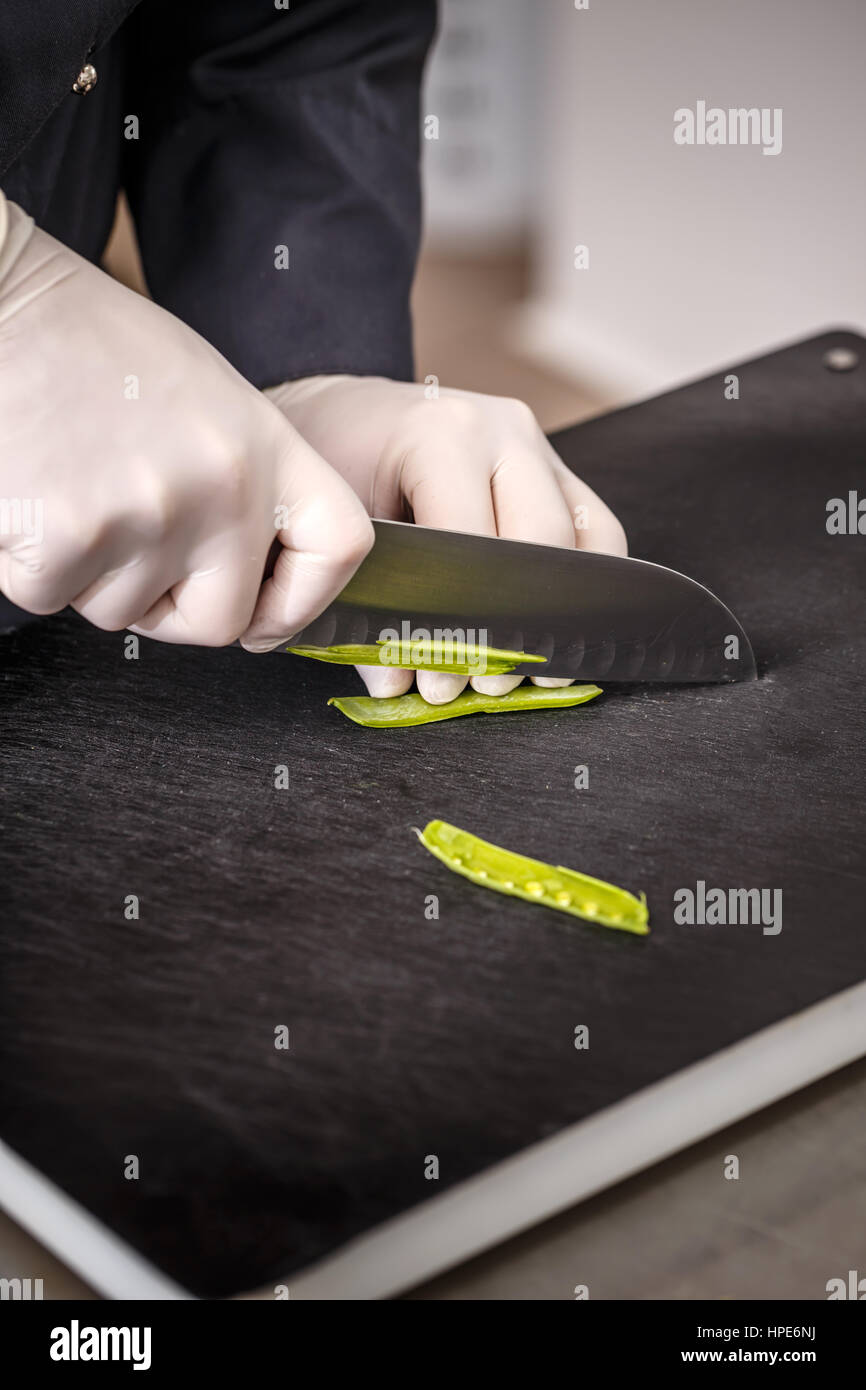 Chef fresco di taglio di piselli verdi su sfondo nero tagliere Foto Stock