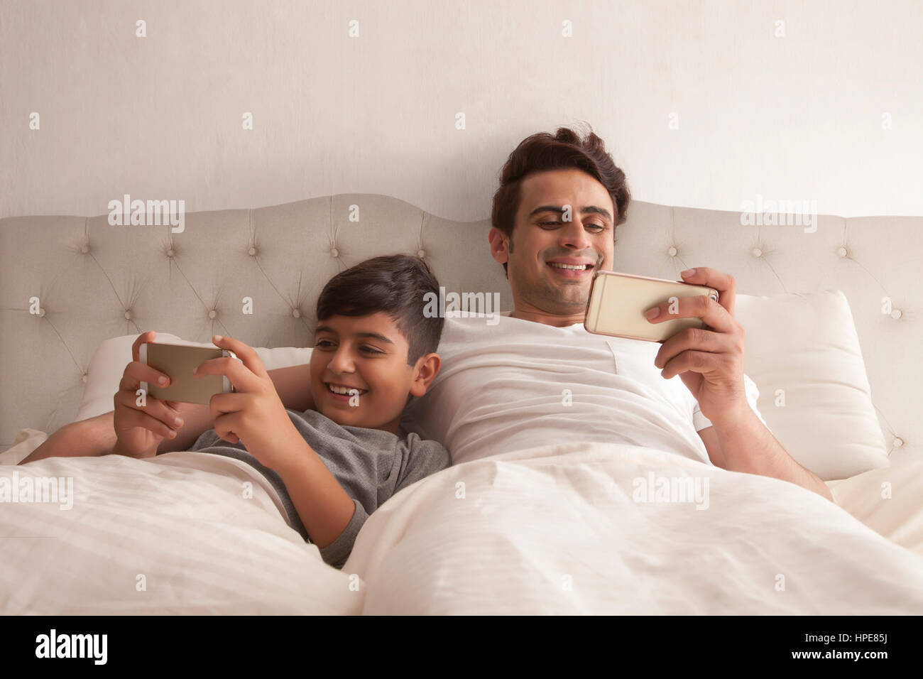 Sorridente padre e figlio utilizzando il telefono cellulare sul letto in camera da letto Foto Stock