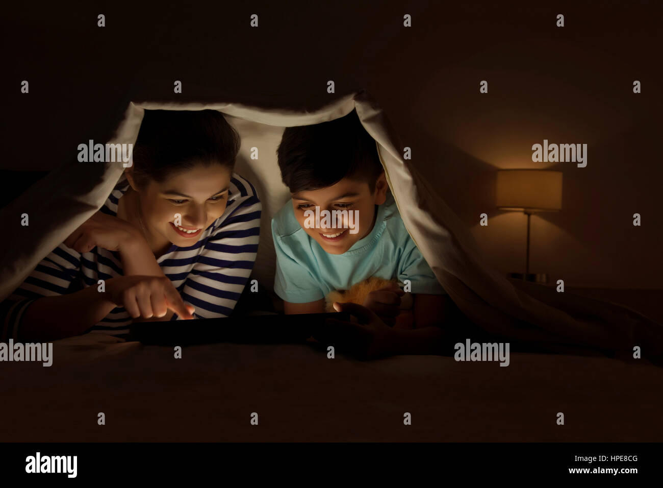 Madre e Figlio la condivisione digitale compressa sotto una coperta di notte in camera da letto Foto Stock